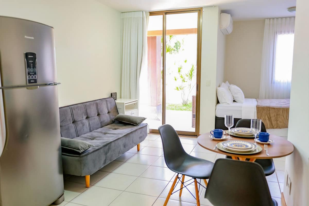 A modern room with a sofa, dining table, chairs, a refrigerator, and a bed with a view.