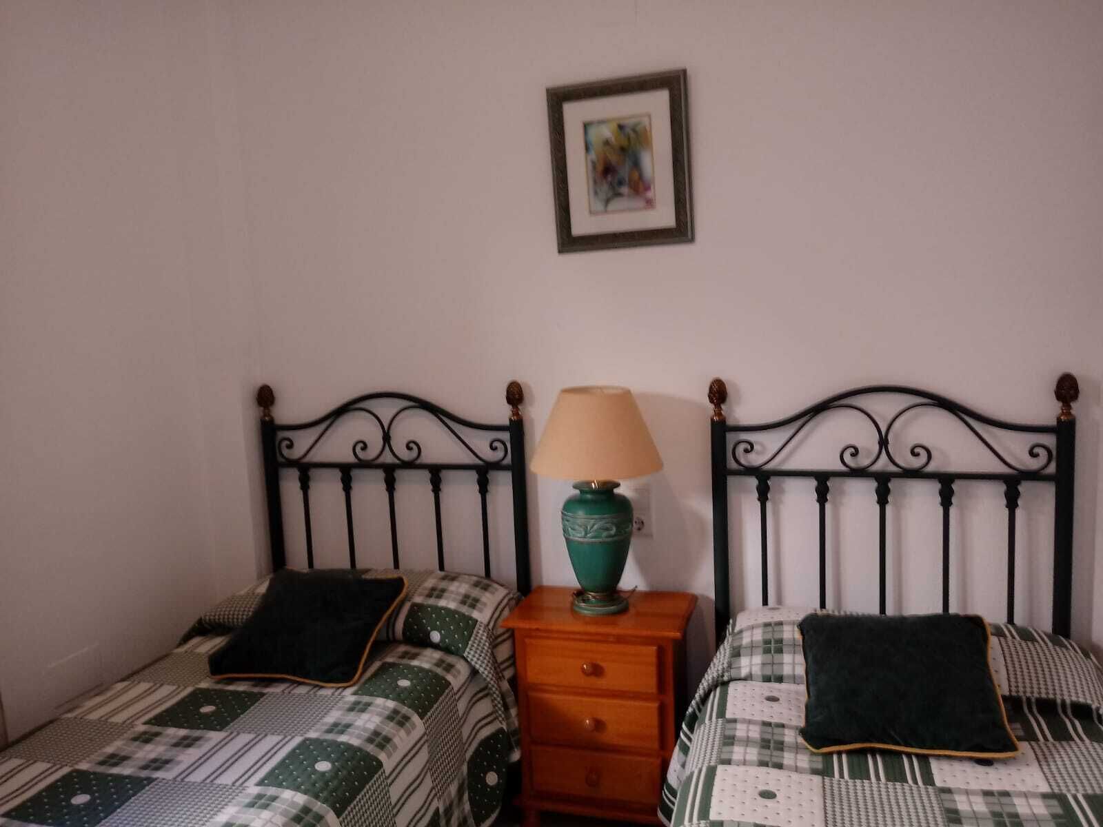 Twee enkele bedden met metalen hoofdborden, een nachtkastje met lamp en een ingelijst beeld aan de muur.