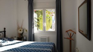 Ein Schlafzimmer mit einem Bett, einem Fenster mit Vorhängen, einem Heizkörper und einem Spiegel an der Wand.