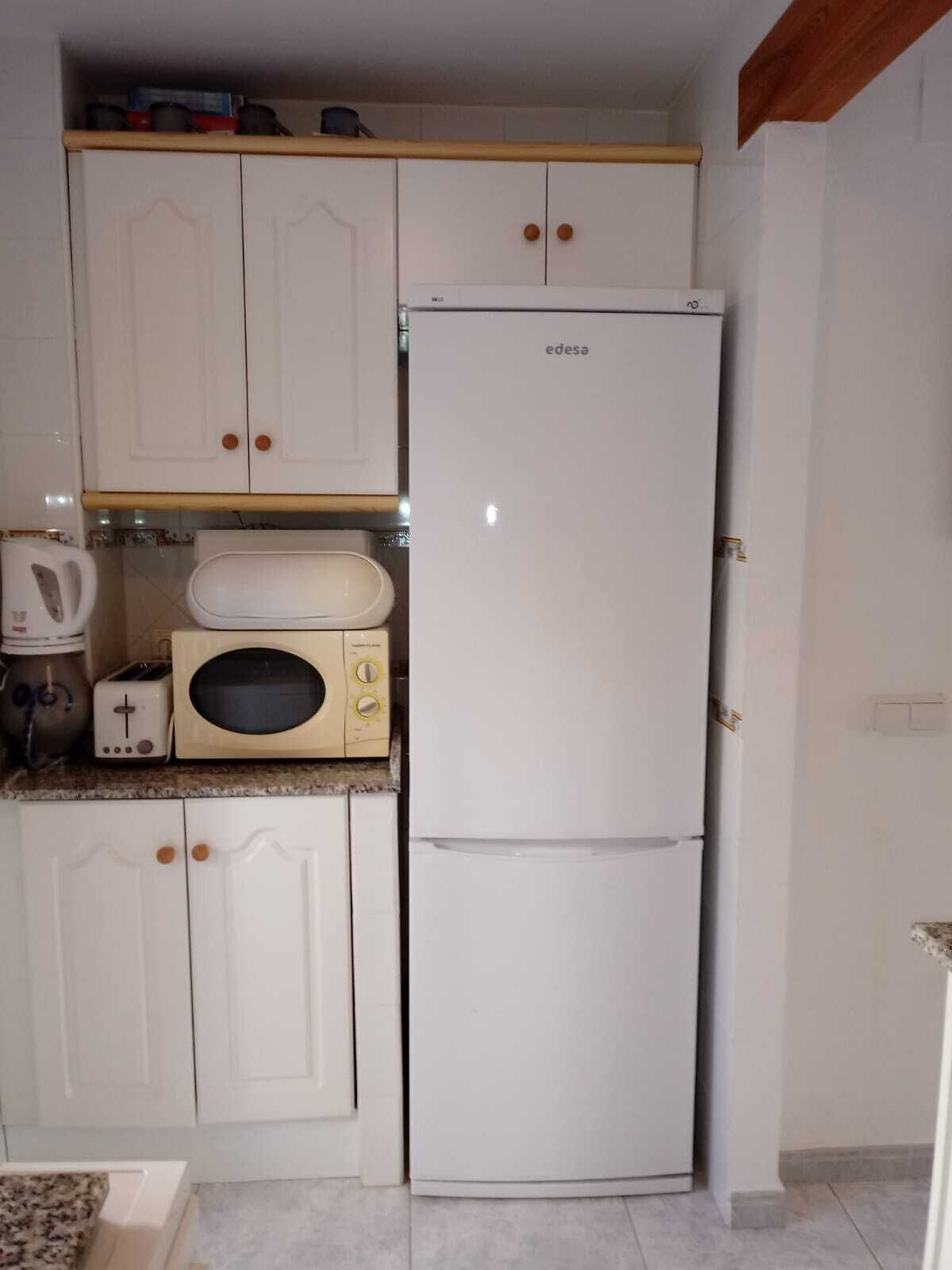 A compact kitchen with white cabinets, a built-in microwave, a toaster, and a white refrigerator.