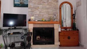 Ein Wohnzimmer mit Flachbildfernseher, Kamin aus Stein, Spiegel und Holzkommode.