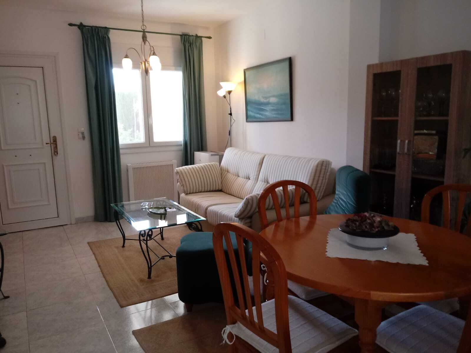 A living room with a sofa, a glass coffee table, a wooden dining table with chairs, a radiator, and a painting on the wall.