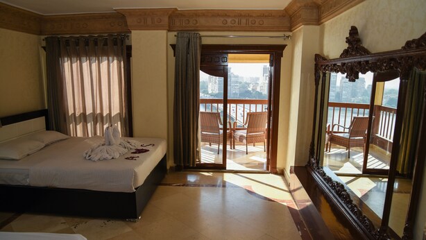 A hotel room with a bed, a balcony with wicker chairs, and a large ornate mirror. - Nile sky hotel and suites (Cairo)