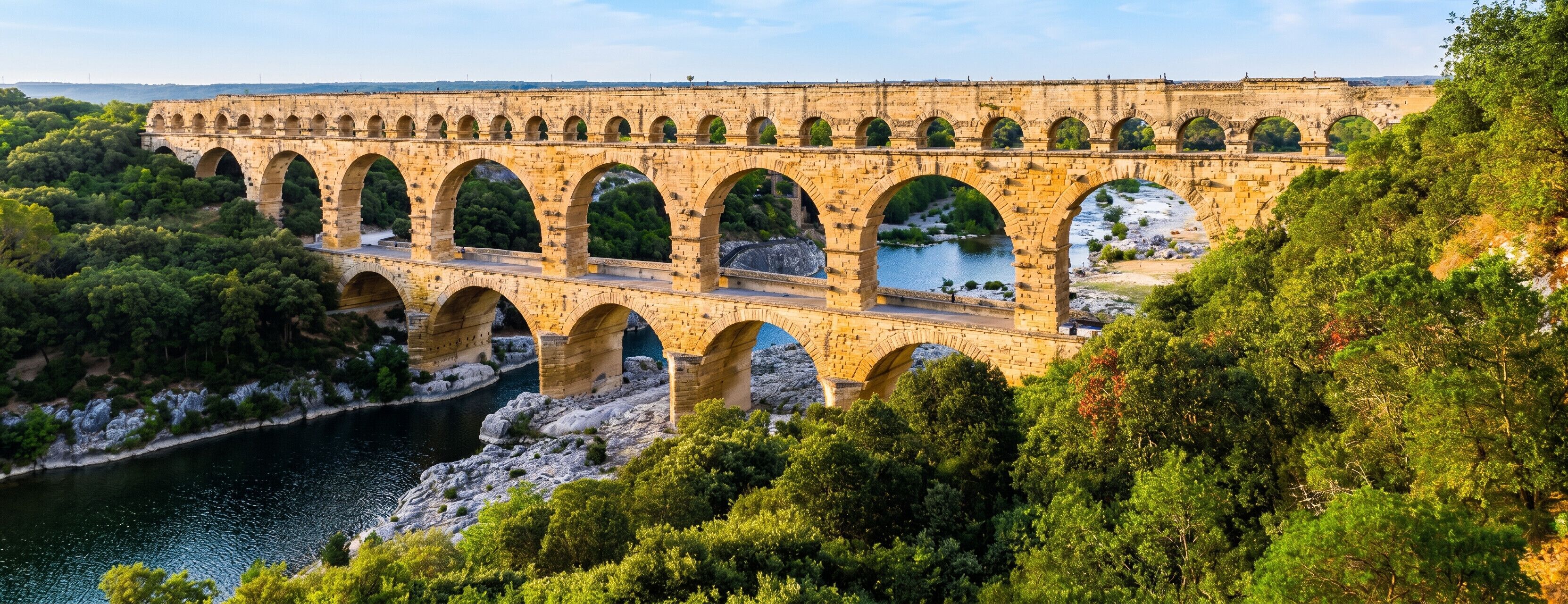 Eine Steinbrücke mit mehreren Bögen überspannt einen Fluss, umgeben von dichtem Grün.