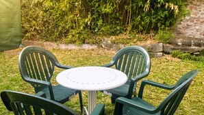 Une table ronde entourée de quatre chaises vertes, le tout installé dans un jardin.