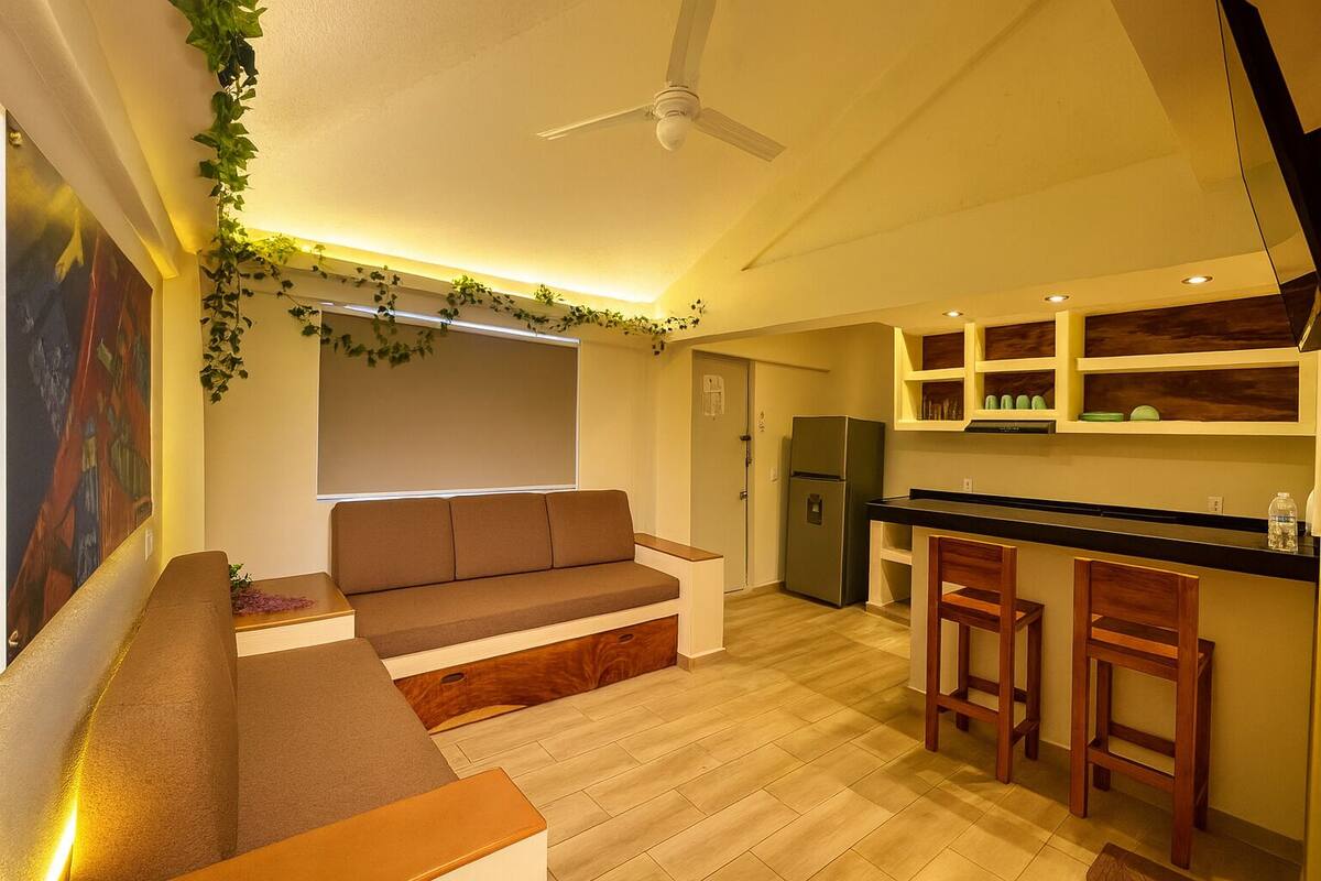A compact living space with a sofa, a small kitchen area, and a ceiling fan.