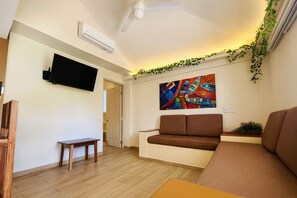 A living room with a brown sofa, a small wooden table, a TV mounted on the wall, and a colorful painting. - Hotel Casa Ixtapa (Ixtapa)