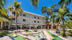 A courtyard with a pool table, palm trees, and a building with multiple balconies. - Hotel Casa Ixtapa (Ixtapa)