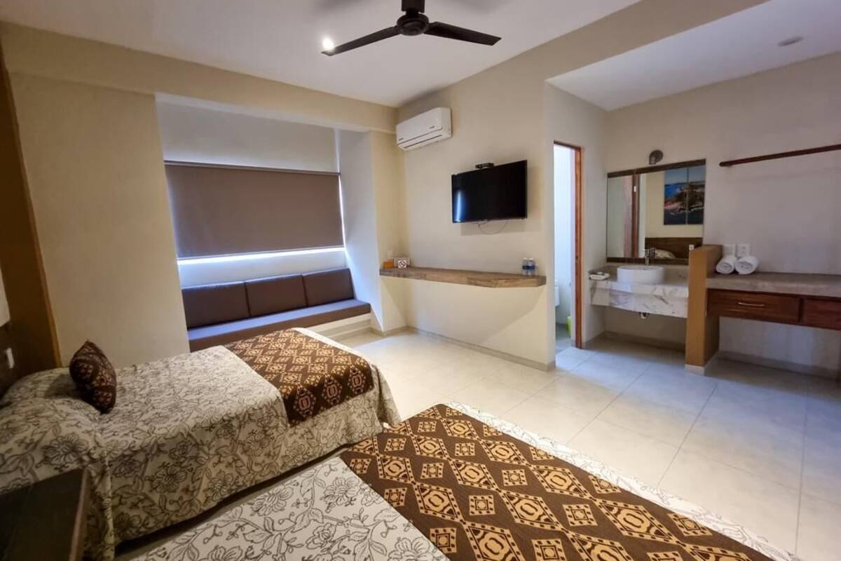 A hotel room with two beds, a television, a bathroom, and a ceiling fan.