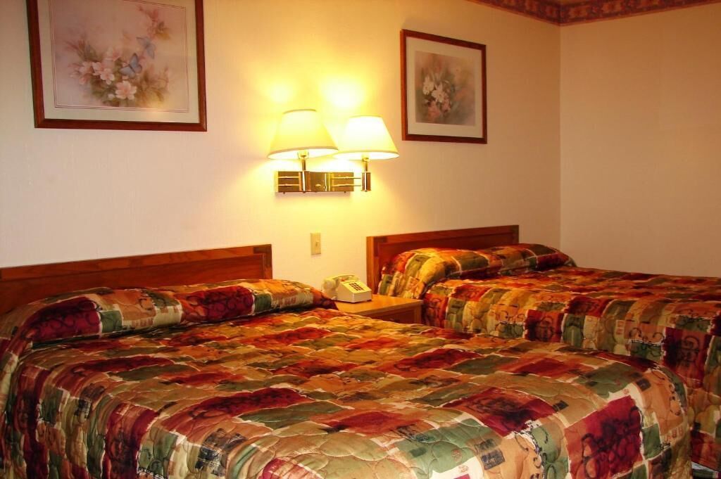 A hotel room with two beds, a nightstand, and wall-mounted lamps.