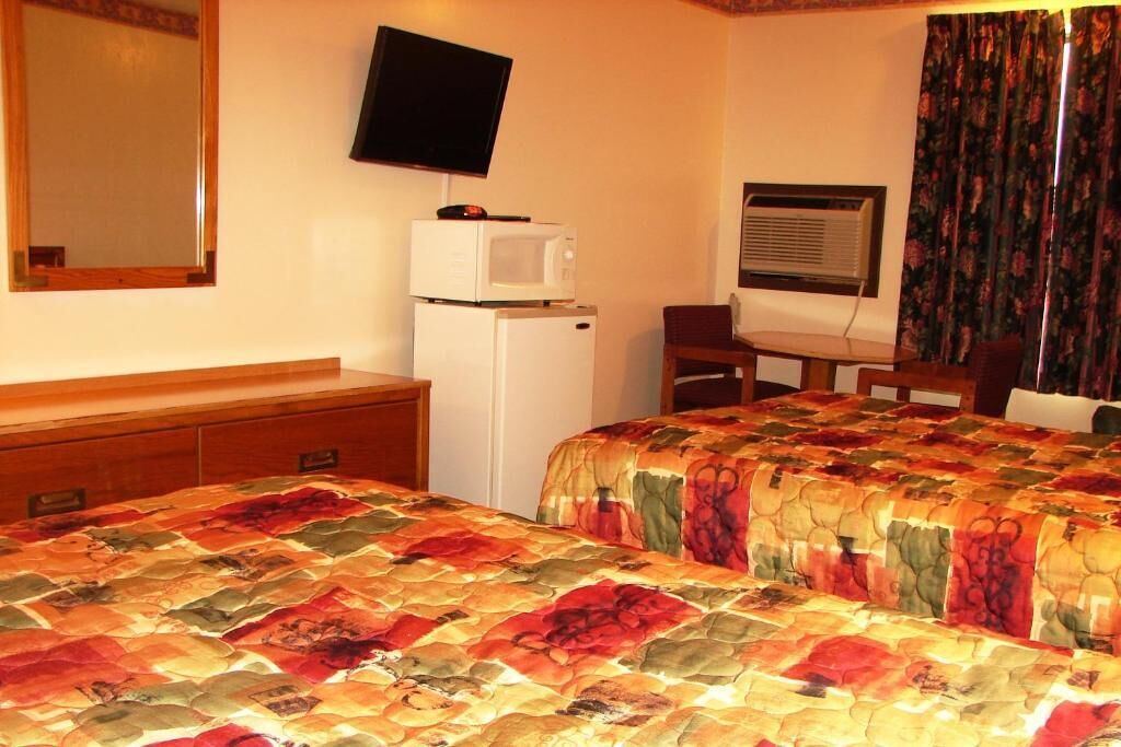 A hotel room with a bed, a desk, a television, a microwave, and an air conditioning unit.