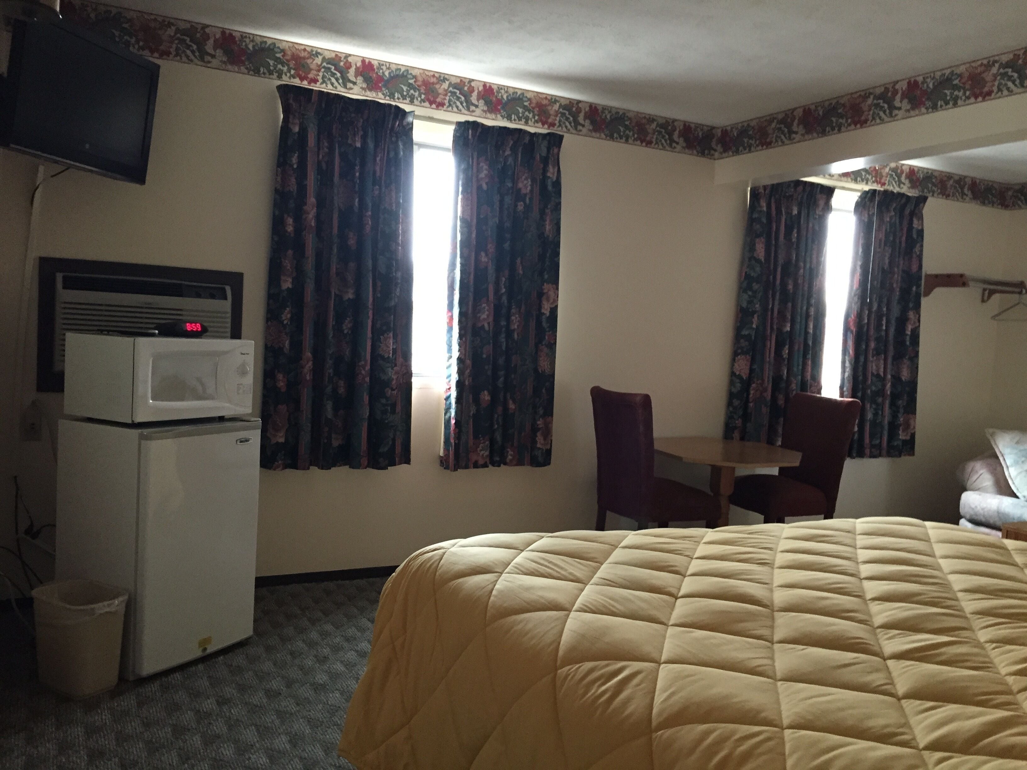 A hotel room with a bed, a desk, a chair, a microwave, and a TV.