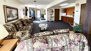 Un vestíbulo de hotel con un conjunto de sofás, una mesa de centro, una lámpara, un cuadro, una puerta y una pequeña zona de kitchenette.