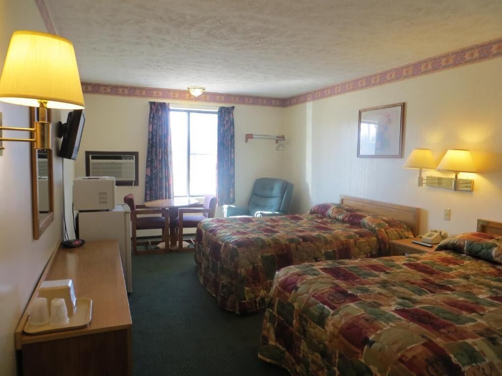 Una camera d'albergo con due letti, una scrivania, una sedia, una televisione e una finestra con tende.