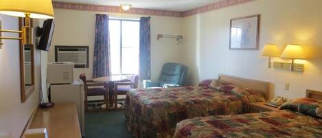 Una camera d'albergo con due letti, una scrivania, una sedia, una televisione e una finestra con tende.