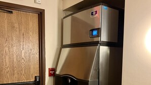 Una kitchenette compacta con refrigerador de acero inoxidable, horno empotrado y microondas.