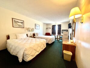 A hotel room with two beds, a desk, a chair, a lamp, a trash bin, and a television.