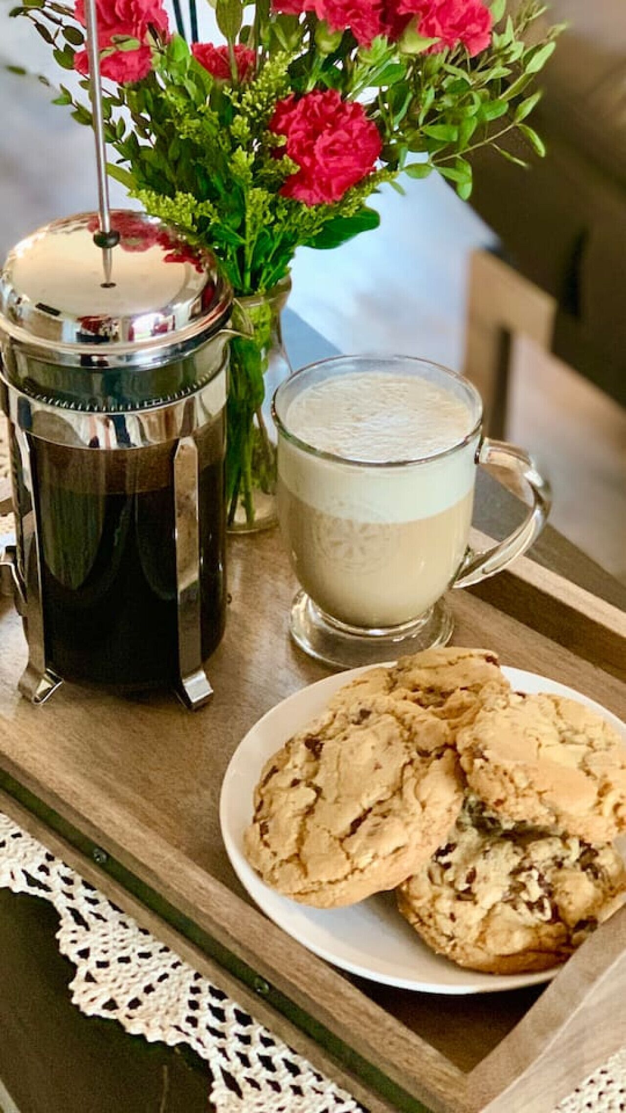 A tray with a coffee pot, a mug of coffee, a plate of cookies, and a vase with flowers.