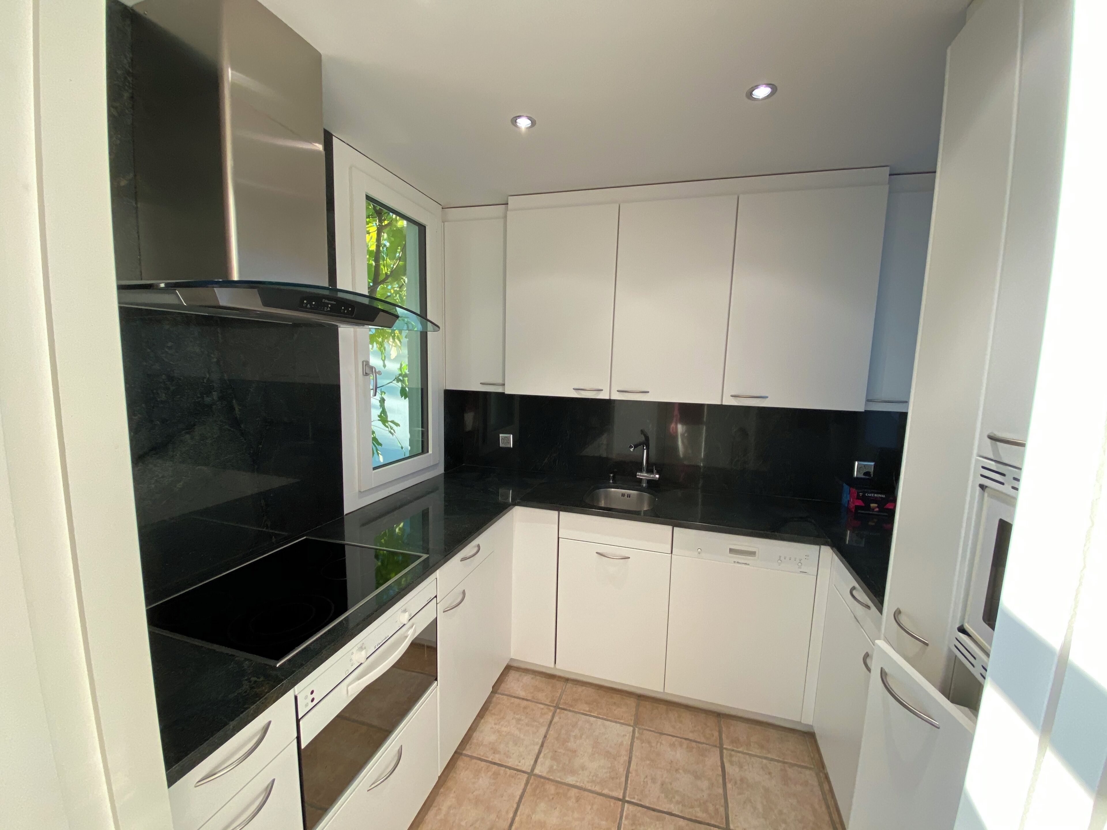 A compact kitchen with white cabinets, a black countertop, and a window with a view of greenery.