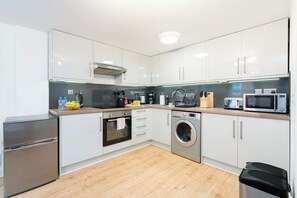 Une cuisine moderne avec des armoires blanches, des appareils électroménagers en acier inoxydable, un four encastré, un lave-linge et un four à micro-ondes.