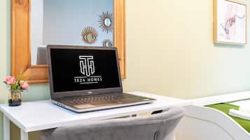 A laptop on a white desk with a vase of flowers, a mirror, and wall art.