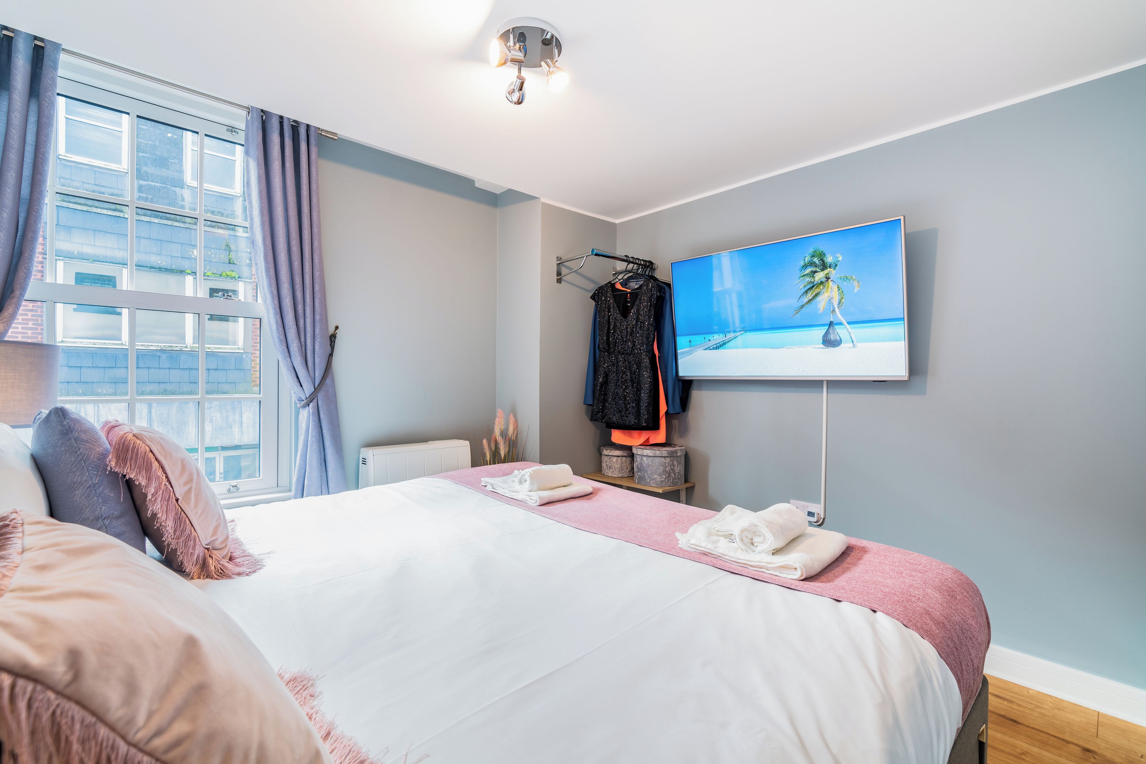 A hotel room with a bed, a TV on the wall, and a window with curtains.