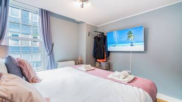 A hotel room with a bed, a TV on the wall, and a window with curtains.