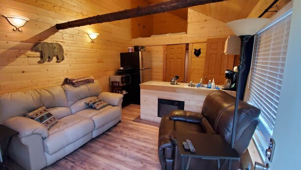 A cozy cabin interior with a sofa, a leather chair, a dining table, and a kitchen area. - Baby Bear Kenai/Soldotna fishing cabin- sleeps 3 - Alaska Building a Dream (Soldotna)