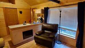 A cozy cabin interior with a wooden interior, a leather chair, a small kitchen area, and a window with blinds. - Baby Bear Kenai/Soldotna fishing cabin- sleeps 3 - Alaska Building a Dream (Soldotna)