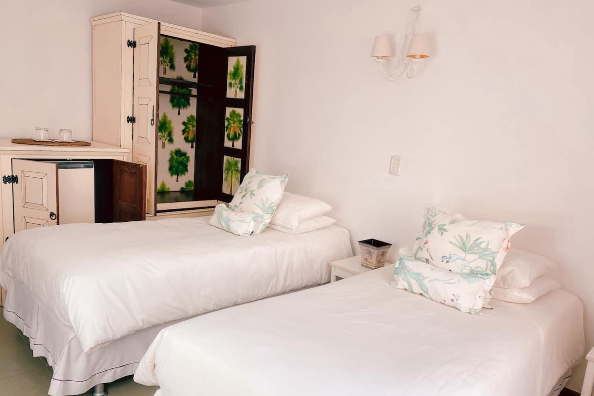 Una habitación con dos camas, un armario, una mesita y una lámpara en la pared.