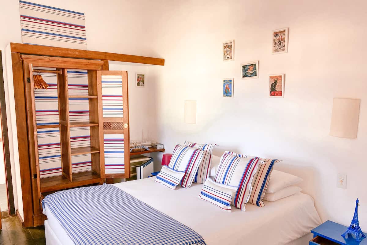 Un dormitorio con una cama grande, almohadas a rayas, una manta de cuadros, un armario de madera y un pequeño modelo de la Torre Eiffel sobre una mesita de noche.
