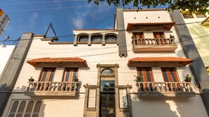 Un edificio con entrada central, balcones con barandillas y un letrero que indica que es un hotel.
