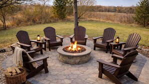 A circular fire pit with four Adirondack chairs around it, set on a stone patio. - Unique Home Where The Buffalo Roam! Perfect for Families, Reunions. Hunters. (Buffalo Ridge)