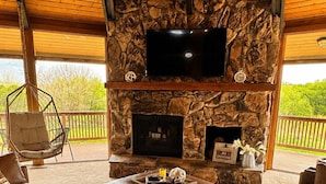 A cozy outdoor living area with a stone fireplace, leather seating, and a flat-screen TV mounted above the hearth. - Unique Home Where The Buffalo Roam! Perfect for Families, Reunions. Hunters. (Buffalo Ridge)