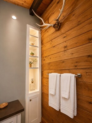 A bathroom with wooden walls, a white door, a shelf with toiletries, and a towel rack.