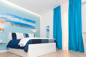 Ein modernes Schlafzimmer mit Stadtbild-Wandgemälde, einem weißen Bett und leuchtend blauen Vorhängen.
