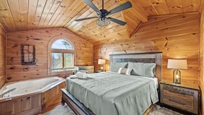 A wooden cabin bedroom with a large bed, a bathtub, and a ceiling fan.