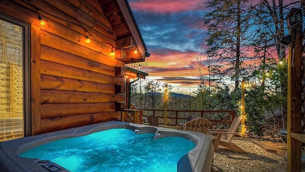 A wooden cabin with a hot tub and deck chairs.