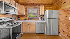 A compact kitchen with wooden walls, a stainless steel refrigerator, a microwave, and a dishwasher.