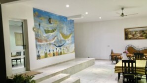 A dining area with a high table and chairs, a staircase leading to another room, and a large abstract painting on the wall. - un séjour inoubliable. Surpresseur, chauffe eau, Clim , piscine, plage … jardin. (Ngaparou)