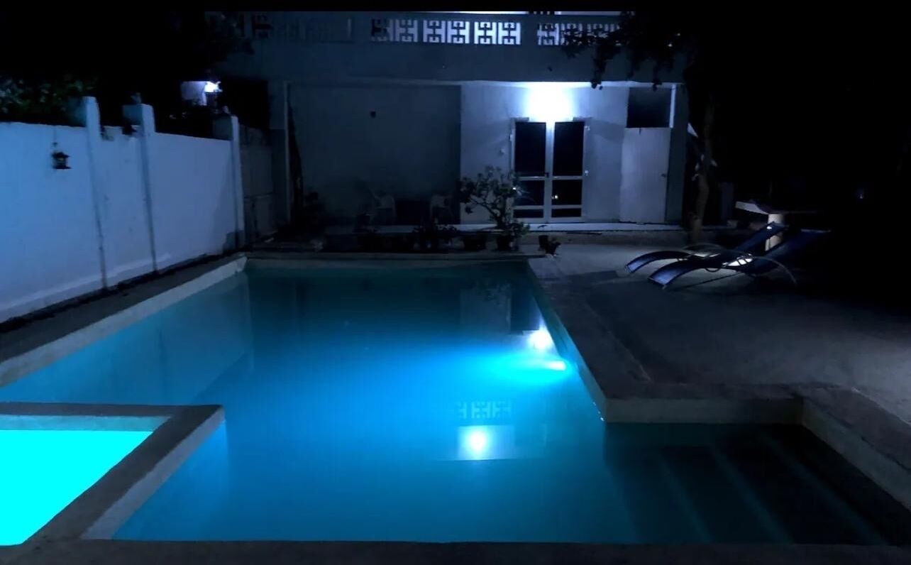 A swimming pool at night with illuminated edges and a white fence surrounding it.