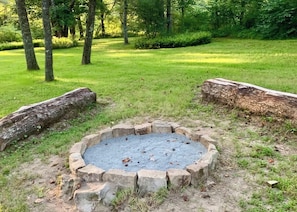 A circular stone fire pit surrounded by a stone border, set in a grassy area with trees in the background.