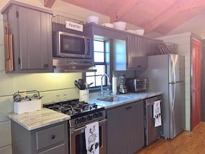 A kitchen with grey cabinets, a stainless steel stove, a microwave, a refrigerator, and a sink.