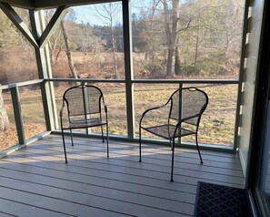 A covered porch with two metal chairs and a view of a wooded area. - Charming Cabin Near Falls, Hiking, & Fly-Fishing (Brevard)
