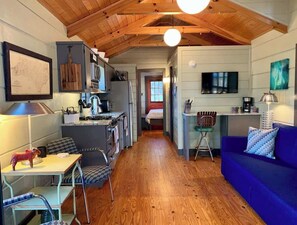 A cozy interior with a wooden ceiling, a dining area with a table and chairs, a kitchen with a stove and refrigerator, and a living area with a blue sofa.