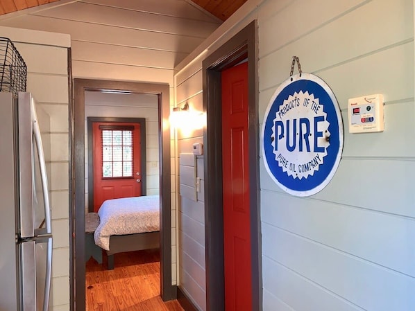 A narrow hallway with a bed, a red door, and a sign reading "PURE".