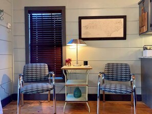 A room with two patterned chairs, a small table with a lamp, a map on the wall, and a wooden cabinet.