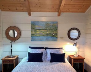 A bedroom with a bed, two bedside tables, two wall-mounted mirrors, and a painting of a landscape.