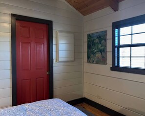 A room with a red door, a window with blinds, and a painting on the wall. - Charming Cabin Near Falls, Hiking, & Fly-Fishing (Brevard)