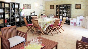 A dining area with a table set for six, surrounded by wooden chairs with pink cushions. There are wine bottles and glasses on shelves and a wine rack. - Lovely apartment in villa for 5 people with WIFI and TV (Jau-dignac-et-loirac)